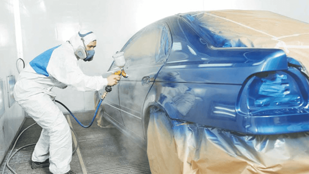 Man spraying blue paint on a car in a spray paint shop.