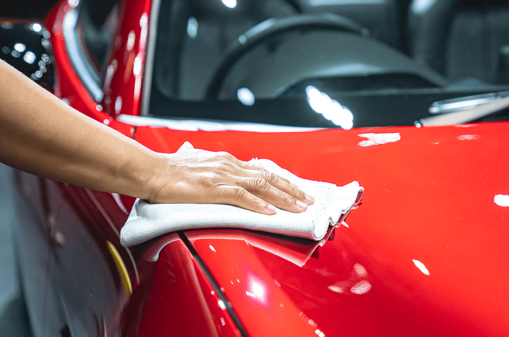 A smooth and shining hood of a car being wiped by a person of around mid 30s with a white towel.